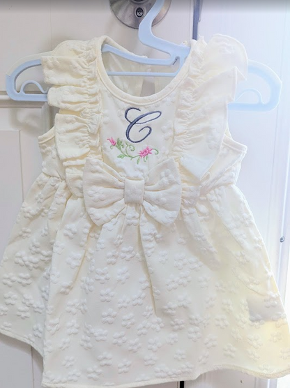 White baby dress with a bow and embroidered monogram letter 'C' on a hanger.
