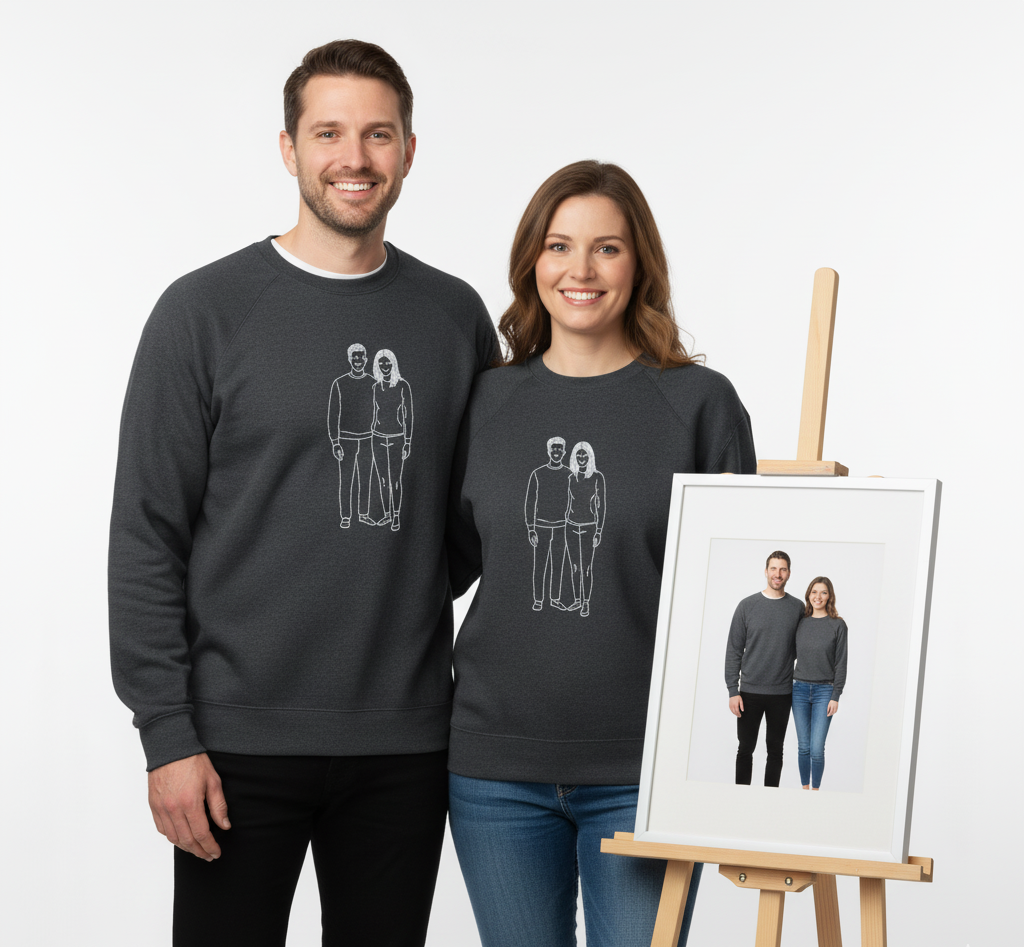 Two people wearing matching black sweatshirts with a graphic of themselves embroidered on the sweatshirt, standing next to an easel with a framed picture of the same scene.