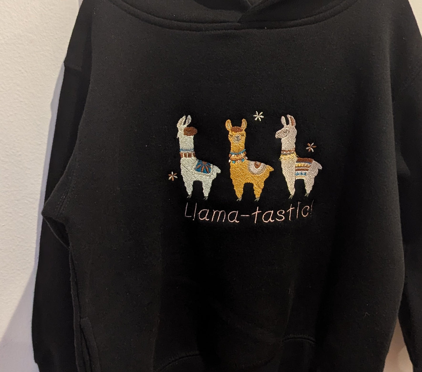 Black hoodie with embroidered llamas in beautiful threads and 'Llama-tastic!' text on a plain background