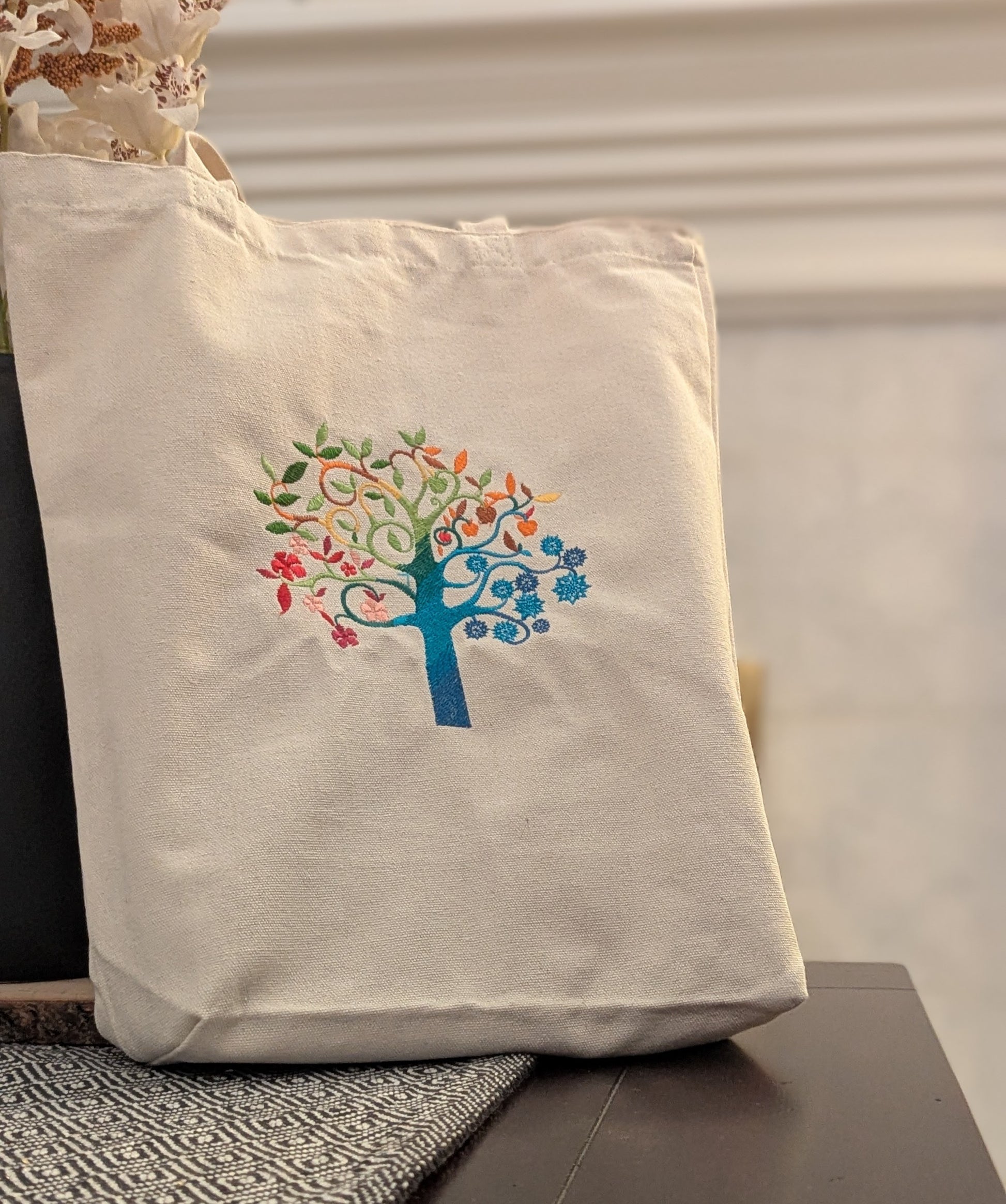 Beige tote bag with a colorful tree design on a neutral background