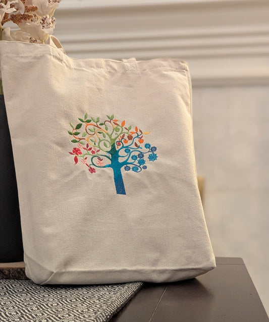 Beige tote bag with a colorful tree design on a neutral background