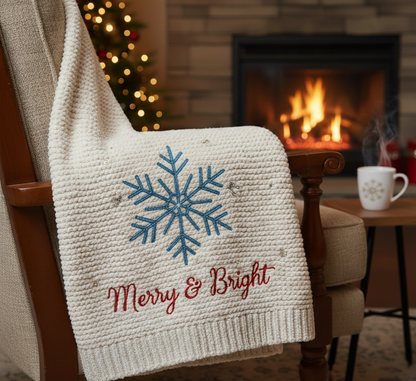 Knitted blanket with snowflake design and 'Merry & Bright' text embroidered on it draped over a chair in front of a fireplace.