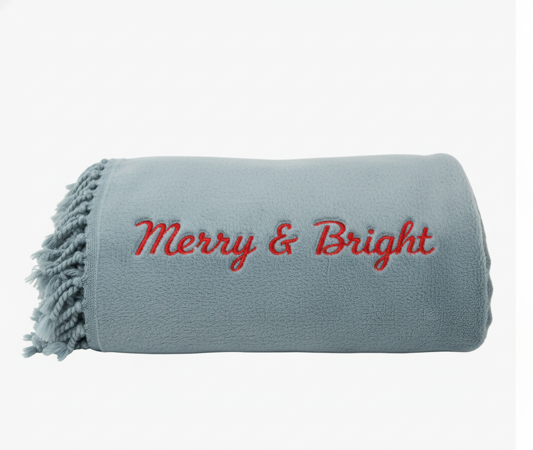 Gray blanket with 'Merry & Bright' text embroidered on a white background