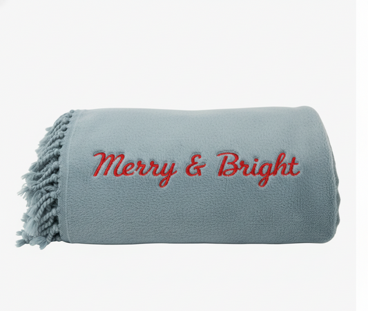 Gray blanket with 'Merry & Bright' text embroidered on a white background