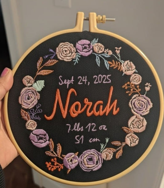Embroidery hoop with floral design and text about birth stats on a black background